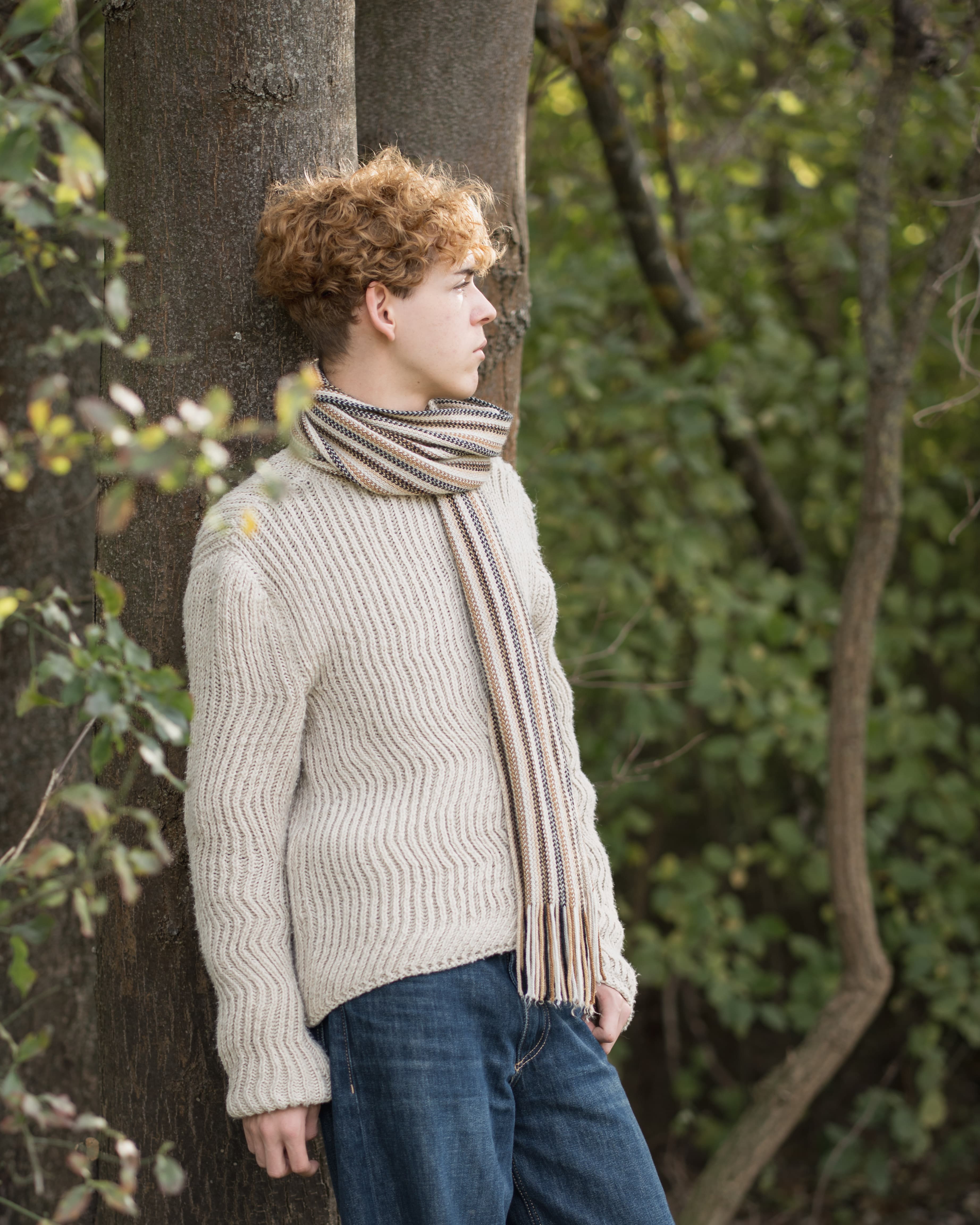 Junger Mann im Wald, Ganzkörperportrait an einem Baum gelehnt